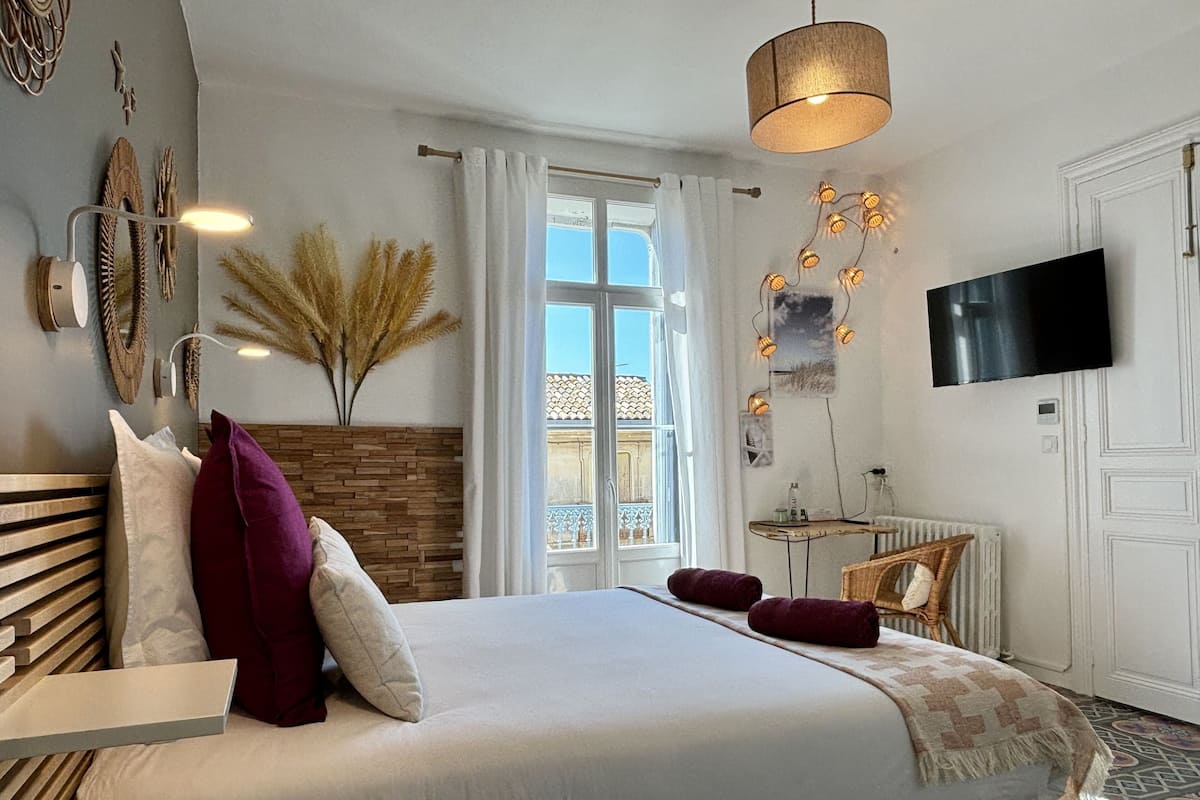 Un dormitorio con cama, televisión, ventana y lámpara fijada a la pared.