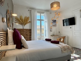 A bedroom with a bed, a TV, a window, and a wall-mounted light fixture.