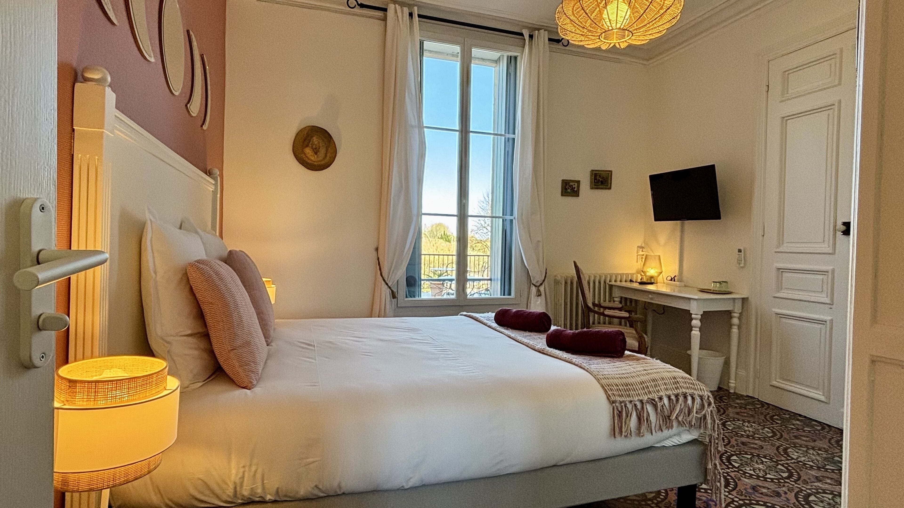 Une chambre à coucher avec un lit, un bureau, une télévision et une fenêtre avec des rideaux.