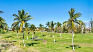Un campo da golf con un percorso ben definito, palme e un edificio sullo sfondo.