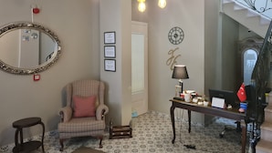 A room with a checkered armchair, a small round table, a desk with a lamp, a mirror, and a staircase with a decorative railing. - Harakop Otel (Ayvalik)