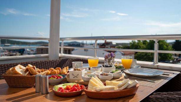 A breakfast table with various food items and drinks, set on a balcony with a view of the city and mountains. - Harakop Otel (Ayvalik)