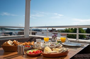 A breakfast table with various food items and drinks, set on a balcony with a view of the city and mountains. - Harakop Otel (Ayvalik)