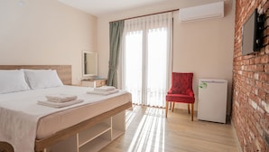 A hotel room with a bed, a nightstand, a TV, a red chair, and a small refrigerator. - Harakop Otel (Ayvalik)