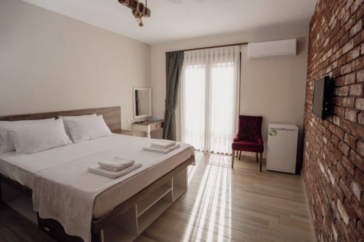 A hotel room with a large bed, a small desk, a chair, a television, and a brick wall.