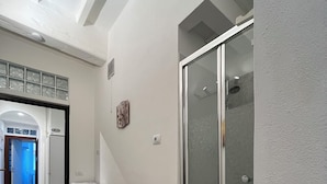 Un pasillo con cabina de ducha de vidrio, un electrodoméstico y un reloj en la pared.