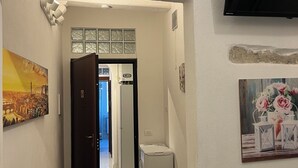 Un pasillo con piso de madera, una puerta que da a una habitación, un televisor montado en la pared y un cuadro en la pared.