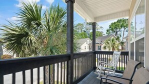 A covered porch with a railing, outdoor seating, and a view of a residential area with houses and palm trees. - Blue Dog Inn - Game Room/Entertainment Room (Brunswick)