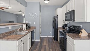 A modern kitchen with granite countertops, white cabinets, a black refrigerator, and a microwave. - Blue Dog Inn - Game Room/Entertainment Room (Brunswick)