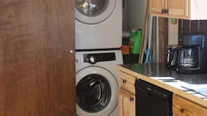 A compact kitchen with wooden cabinets, a dishwasher, a coffee maker, and a washing machine.