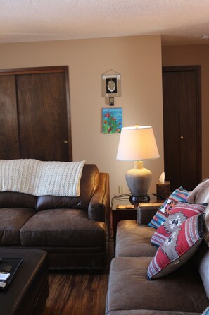 A living room with two brown leather sofas, a white knitted blanket, a lamp, and a wall clock.