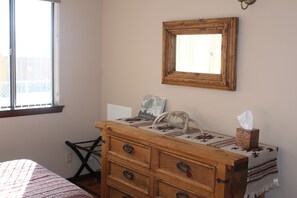 A bedroom with a wooden dresser, a mirror, a window, and a bed with a patterned bedspread.