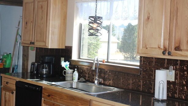 A kitchen with wooden cabinets, a stainless steel sink, a coffee maker, and a window with a view of greenery outside.