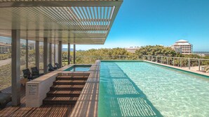 A rooftop pool with clear water, wooden deck, and a covered seating area.