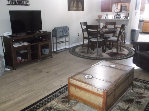 A living room with a wooden coffee table, a television, a dining table with chairs, and a kitchen area in the background.