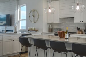 A modern kitchen with white cabinetry, a large island with bar stools, a wine bottle, and pendant lighting.