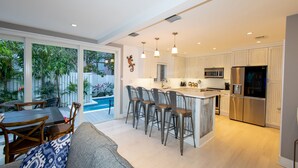 Une cuisine moderne dotée d’un îlot central, de tabourets de bar et d’un coin repas avec vue sur la piscine.