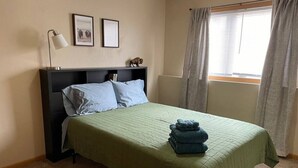 Een slaapkamer met een bed, nachtkastje, lamp en een raam met gordijnen.