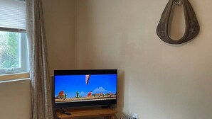 Een televisie op een houten standaard in een kamer met een raam, gordijn en een wandlamp.