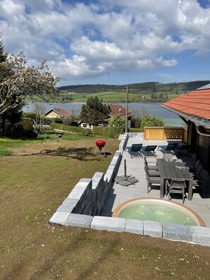 Un espace patio doté d’un jacuzzi, de mobilier d’extérieur et offrant une vue sur un lac et des collines.