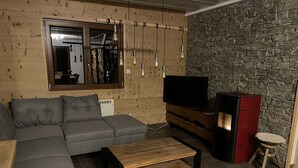 Un salon moderne avec un canapé d’angle, une table basse en bois, un téléviseur à écran plat et un mur en pierre.