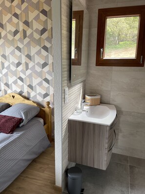 A bedroom with a geometric-patterned wall, a bed with pillows, a bedside table, and a window with a view of greenery. - CHALET WITH SPA AND LAKE VIEW (Montperreux)