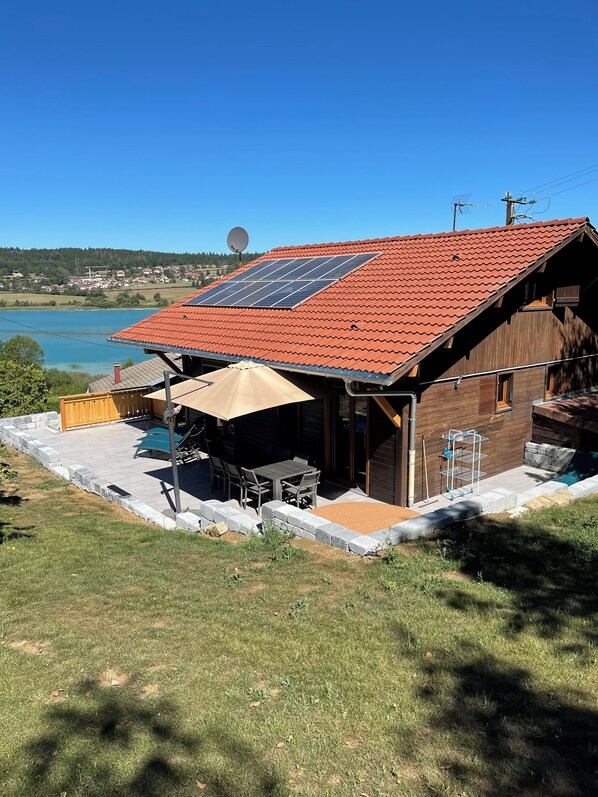 Une maison avec un toit recouvert de tuiles rouges, un panneau solaire, une antenne parabolique et une vue sur un lac.