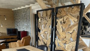 Une table à manger en bois, surmontée de sets de table noirs, entourée de chaises noires, dans une pièce dotée d’un mur en pierre et de poutres en bois.