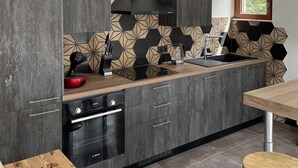 Une cuisine moderne avec des meubles de couleur bois foncé, une hotte noire, un dosseret en carreaux hexagonaux et un plan de travail en bois.