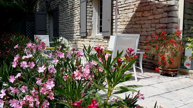 Un edificio in pietra con patio, posti a sedere all'aperto e piante fiorite.