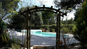 Una pergola in legno con una scala che conduce a una zona piscina, circondata da vegetazione rigogliosa e piante in vaso.