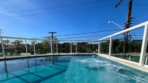 Uma piscina com água azul cristalina, rodeada por uma cerca branca e linhas de energia ao fundo.