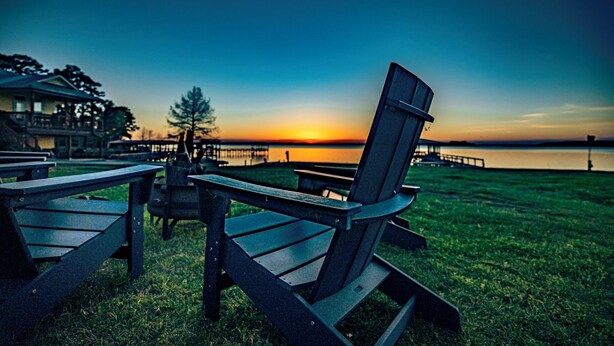 Une vue sur le lac, avec des fauteuils Adirondack et des tables de pique-nique, une jetée et une maison en arrière-plan.
