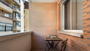 A small balcony with a brick wall, a window, and a wooden table with chairs. - Beautiful apartment, ideal for families in the Aragonese Pyrenees. (Sabiñánigo)