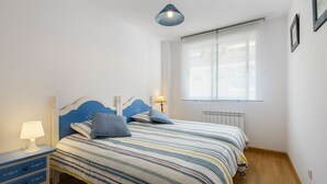 A bedroom with a bed, bedside tables, a lamp, a window, and a radiator. - Beautiful apartment, ideal for families in the Aragonese Pyrenees. (Sabiñánigo)
