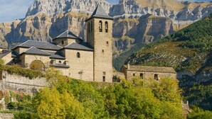 A historic stone building with a bell tower, surrounded by lush greenery and mountains in the background. - Beautiful apartment, ideal for families in the Aragonese Pyrenees. (Sabiñánigo)