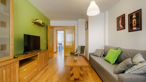 A living room with a TV, wooden cabinets, a sofa with pillows, a coffee table, and a hanging light fixture. - Beautiful apartment, ideal for families in the Aragonese Pyrenees. (Sabiñánigo)
