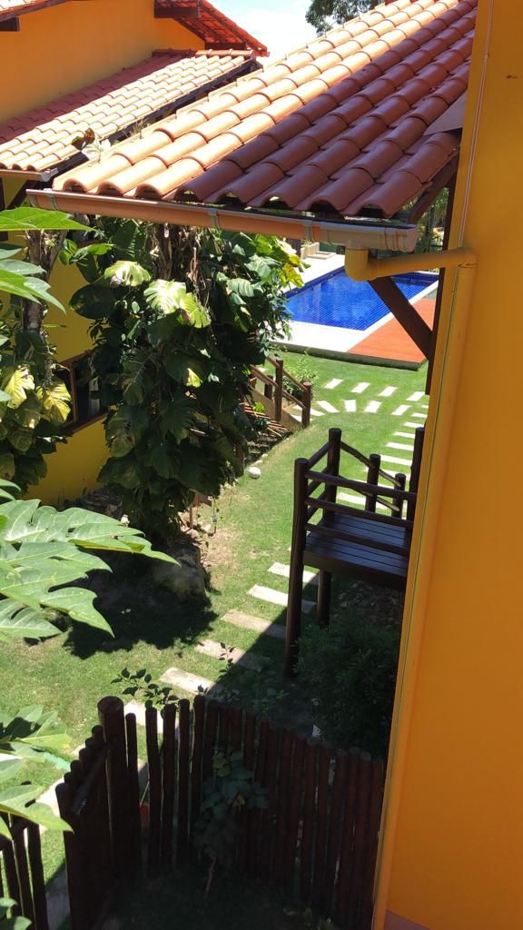 A view of a garden with a wooden fence, a blue pool, and a yellow building with a tiled roof.