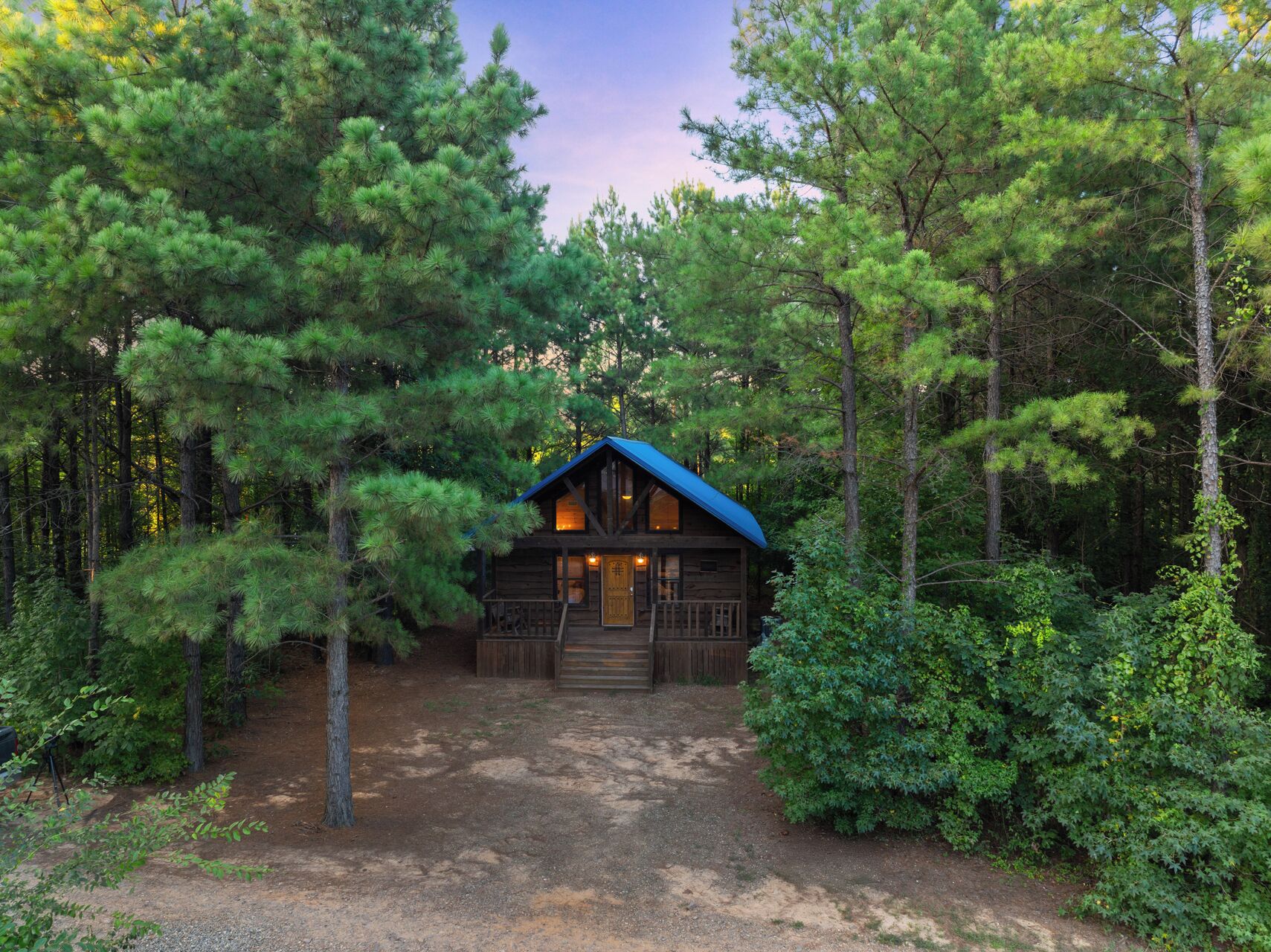 A cabin surrounded by dense forest, with a dirt path leading to the entrance.