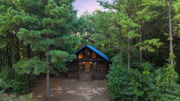 A cabin surrounded by dense forest, with a dirt path leading to the entrance.