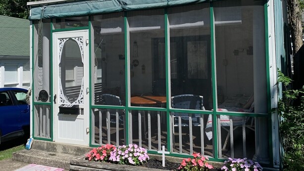 Et hvidt hus med en grøn veranda og en overdækket terrasse.
