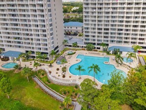 Un hôtel de grande hauteur doté de nombreux balcons, d’une piscine centrale et entouré de verdure.