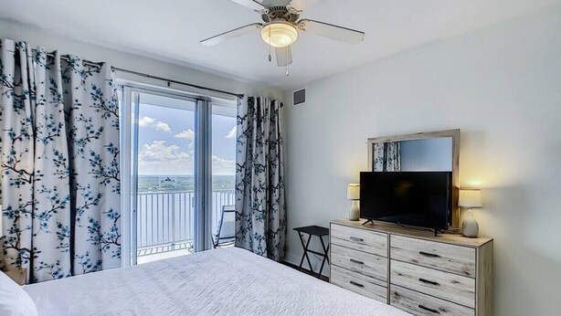 Ein Schlafzimmer mit einem großen Bett, einem Fernseher, einem Schminktisch und einem Balkon mit Vorhängen.