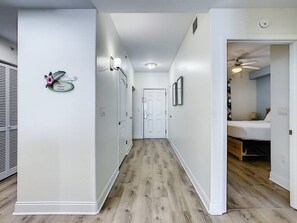 Ein Flur mit Holzboden, weißen Wänden und einer Tür am Ende, die zu einem Schlafzimmer mit Bett und Deckenventilator führt.