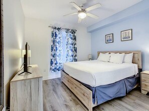 Ein Schlafzimmer mit Bett, Nachttisch, Deckenventilator und einem Fenster mit Vorhängen.