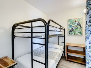 Une chambre avec un lit superposé, une table de chevet en bois et un tableau représentant des oiseaux accroché au mur.