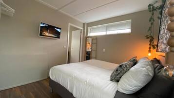 Un dormitorio con una cama, un televisor montado en la pared, una ventana con persianas y una planta.