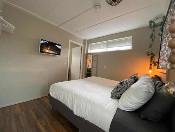 A bedroom with a bed, a television mounted on the wall, a window with blinds, and a plant. - Hakuna Matata (Groningen)