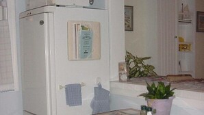 Una cocina compacta con un refrigerador blanco, una pequeña mesa con sillas y una planta en maceta sobre la encimera.