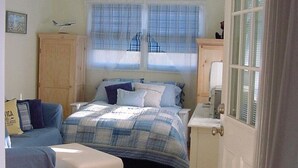 Un dormitorio con cama, escritorio, silla, armario y ventana con persianas.